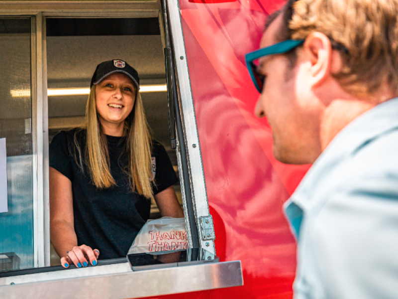 College student working in a red food truck as man approaches